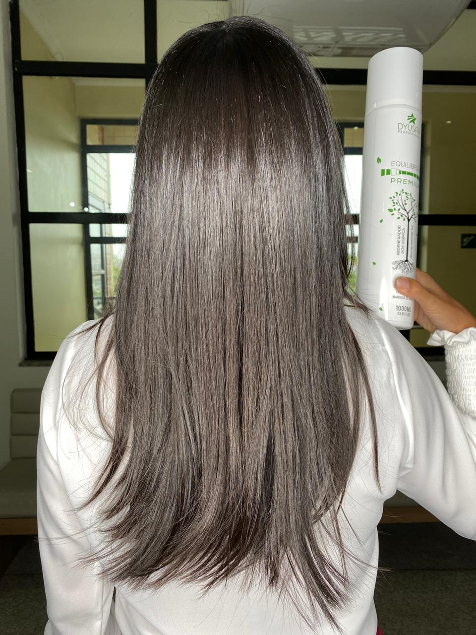 Mulher de costas exibindo cabelo longo, liso e saudavel, segurando o frasco de 1 litro do Regenerador Pos Quimica Equilibrium Premium da Dyusar.
