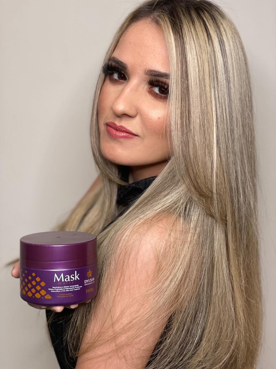 Modelo com cabelo loiro, liso e com luzes, segurando o pote de 300g da Máscara Matizadora Dyusar para manutenção da cor.