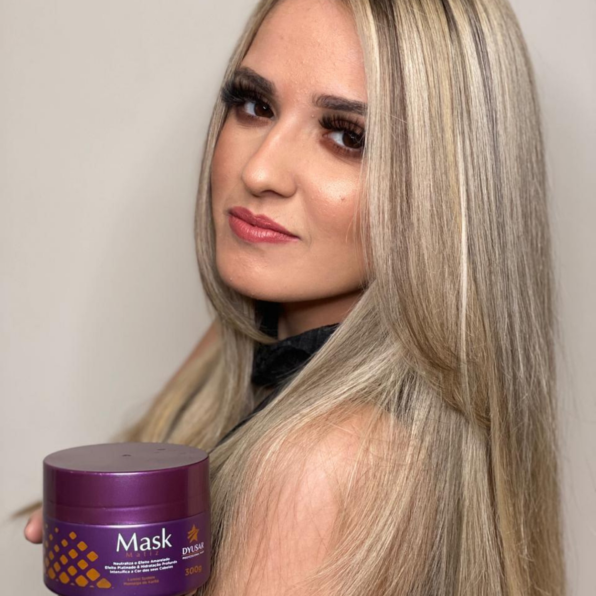 Modelo loira com cabelo platinado segurando a Máscara Matizadora Dyusar, ideal para neutralizar e intensificar a cor.