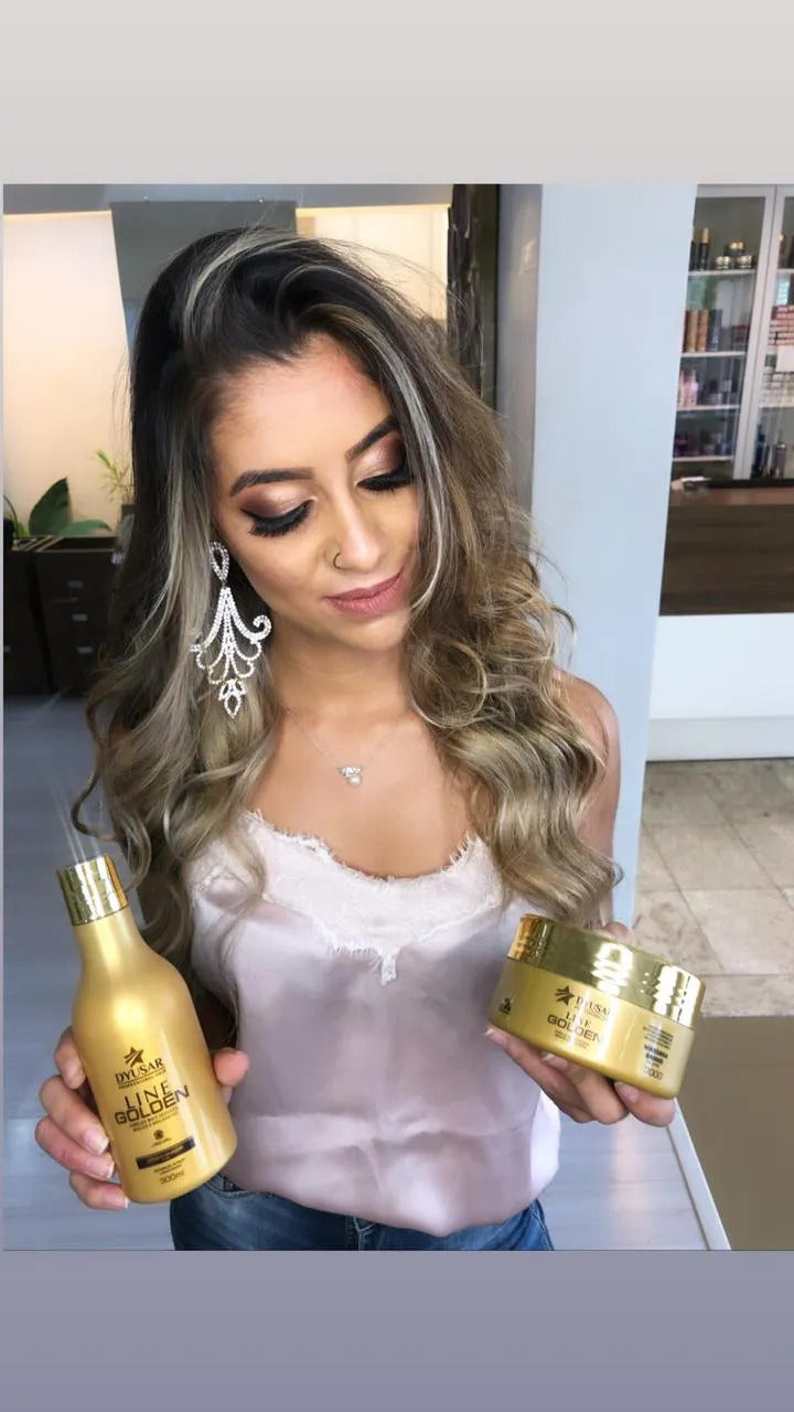 Uma mulher com cabelos ondulados e maquiagem sofisticada segura um frasco de shampoo e o pote da Máscara de Hidratação Dyusar Line Golden, sorrindo.