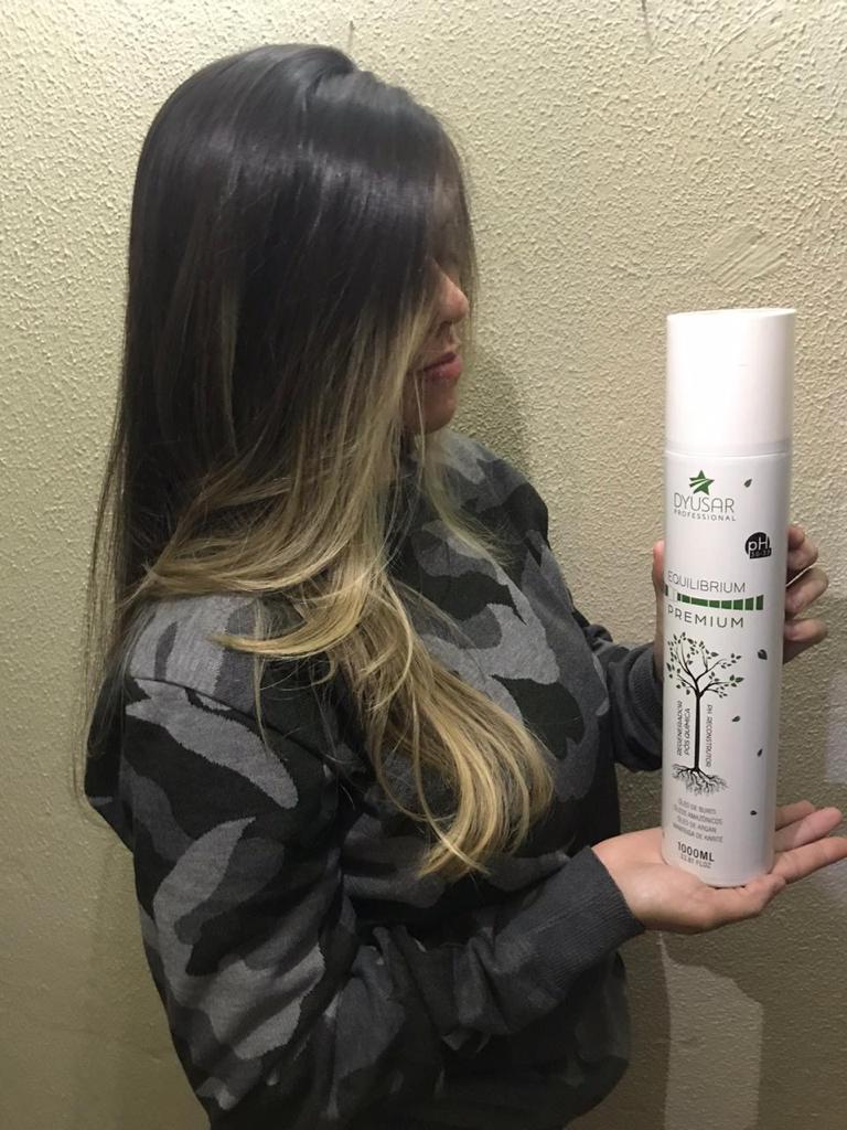 Mulher de costas exibindo cabelo longo, liso e saudavel, segurando o frasco de 1 litro do Regenerador Pos-Quimica Equilibrium Premium da Dyusar.