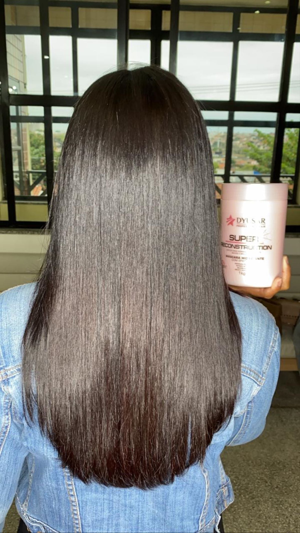 Mulher de costas com cabelo longo, liso e brilhante, segurando a mascara Super Reconstruction do kit de cauterizacao profissional Dyusar.