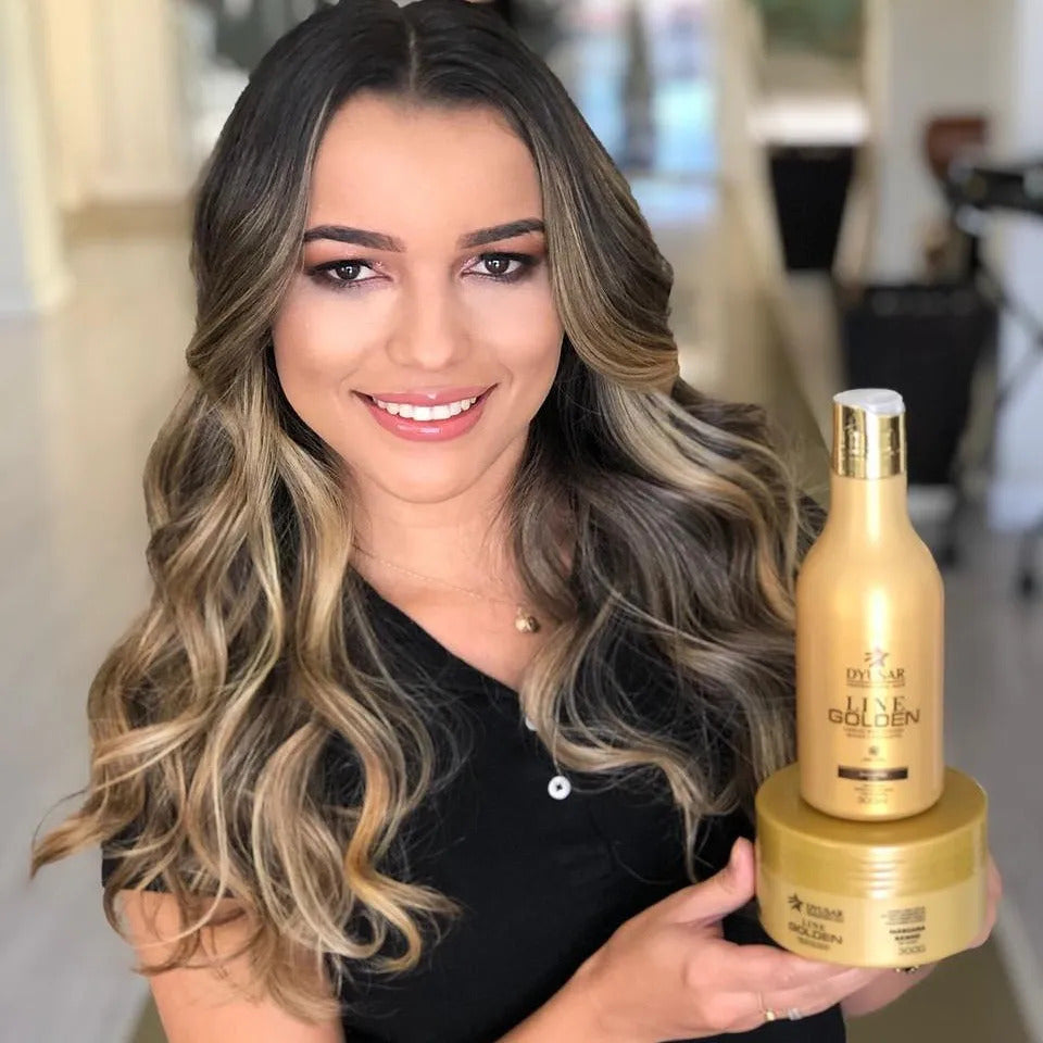 Modelo sorrindo com cabelo longo e ondulado segura o kit com a Máscara de Hidratação Dyusar Line Golden e o shampoo da mesma linha.