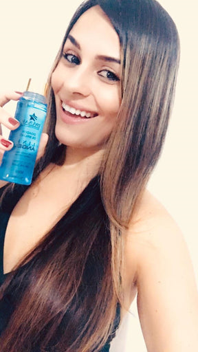 Mulher sorridente com cabelo liso e com mechas, segurando o frasco do Spray de Brilho e Perfume Capilar Line Angel.