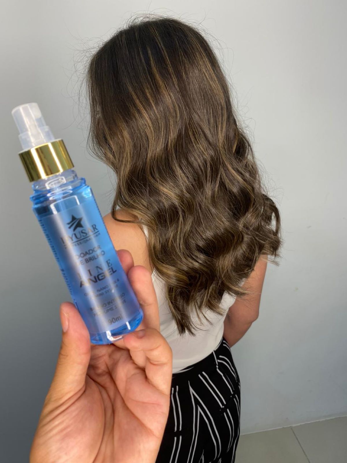 Mão segurando o frasco do Doador de Brilho Line Angel em frente a um cabelo ondulado com luzes, mostrando o brilho final do kit de reconstrução capilar.