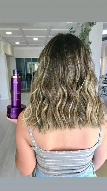 Mulher de costas em um salão, mostrando o resultado de seu cabelo médio, ondulado e com luzes, enquanto segura o Kit de Nutrição com Caviar da Dyusar.