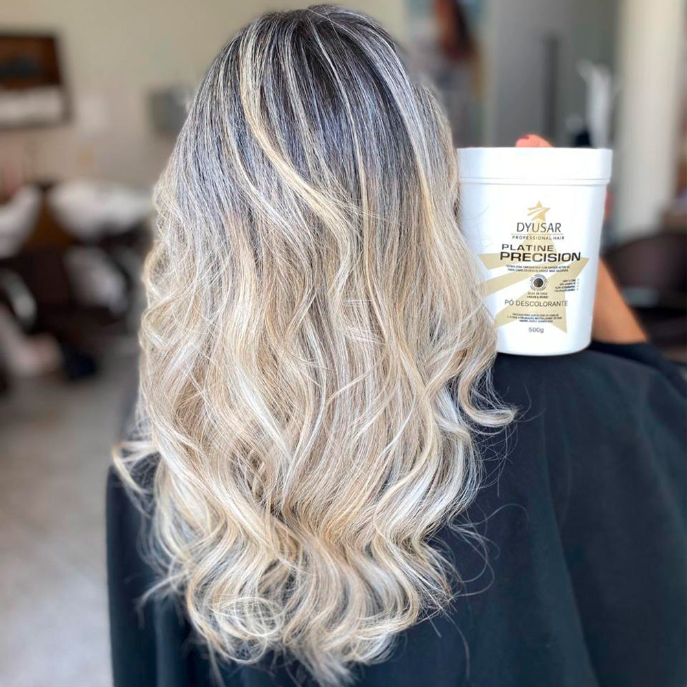 Mulher de costas com cabelo loiro platinado e ondulado, segurando o pote do Pó Descolorante Azul Dyusar.