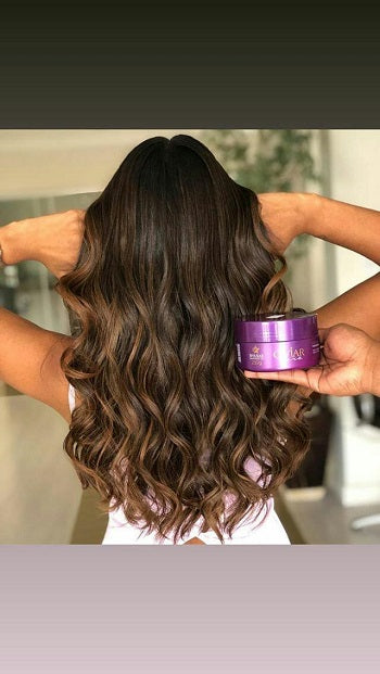 Cabelo longo, castanho e ondulado, com pontas mais claras, sendo exibido enquanto se segura o pote da Máscara de Nutrição com Caviar da Dyusar.