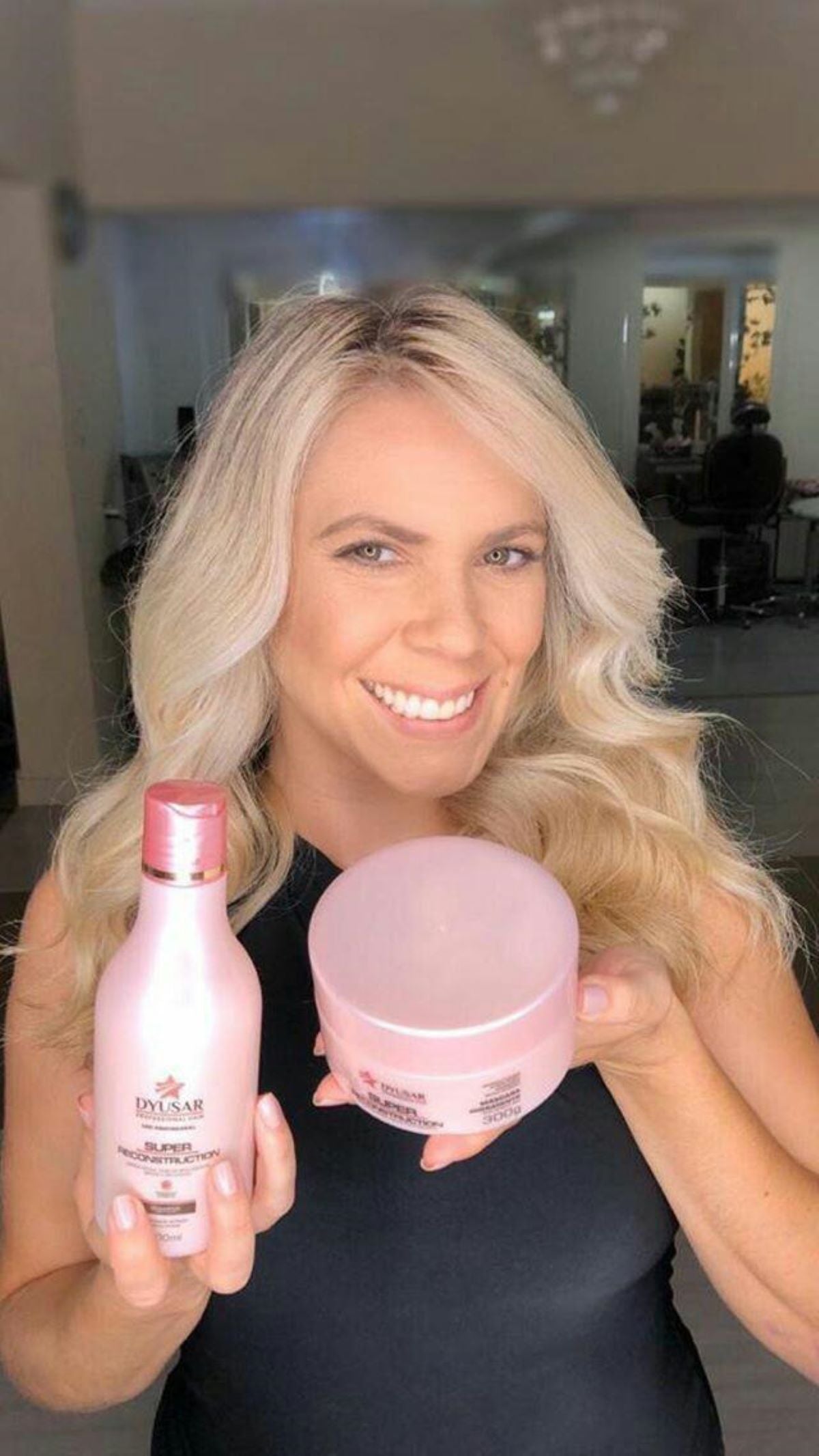 Modelo loira sorrindo e segurando o Condicionador e a Máscara do Kit Home Care Super Reconstruction.