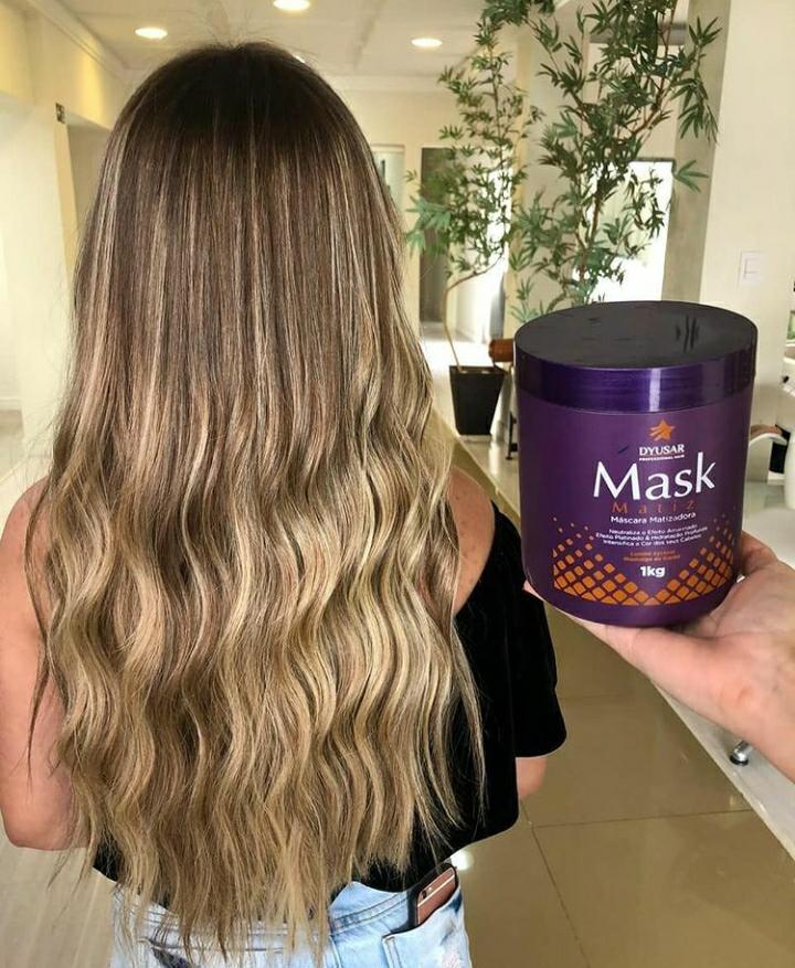 Resultado de um cabelo loiro com luzes, longo e ondulado, com o tom neutralizado e brilhante, ao lado do pote de 1kg da Máscara Matizadora Dyusar.