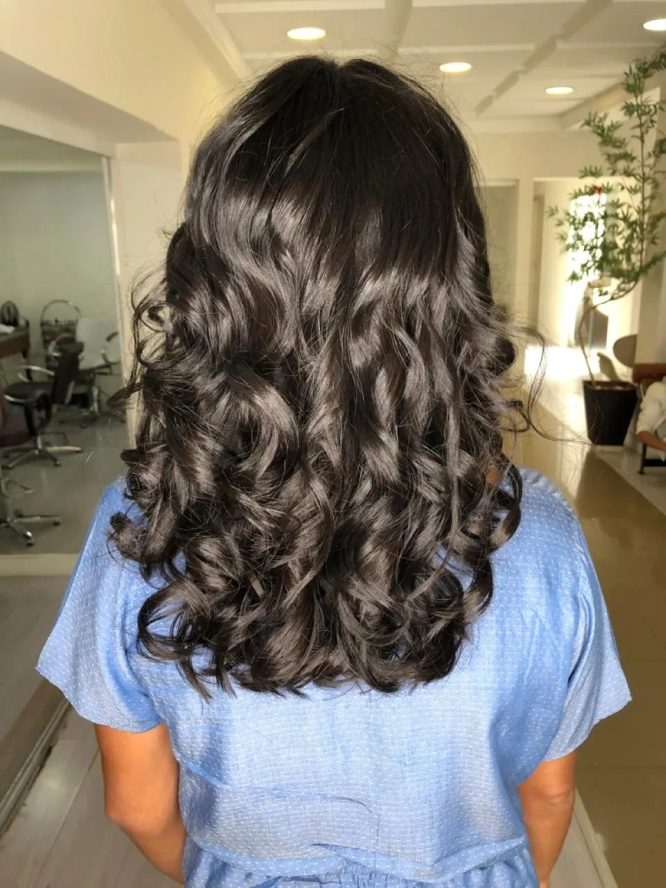 Cabelo cacheado escuro, de comprimento médio, com cachos definidos e muito brilho, mostrando o resultado do tratamento com a Queratina Líquida da Dyusar, que repõe a Cistina nos fios.