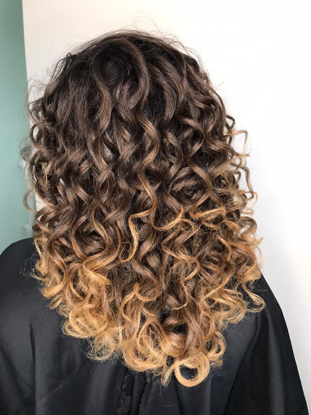 Cabelo cacheado de uma mulher vista de costas, com mechas ombré e cachos perfeitamente definidos e brilhantes após o uso do Creme de Pentear Para Cachos da linha Perfect Curly.